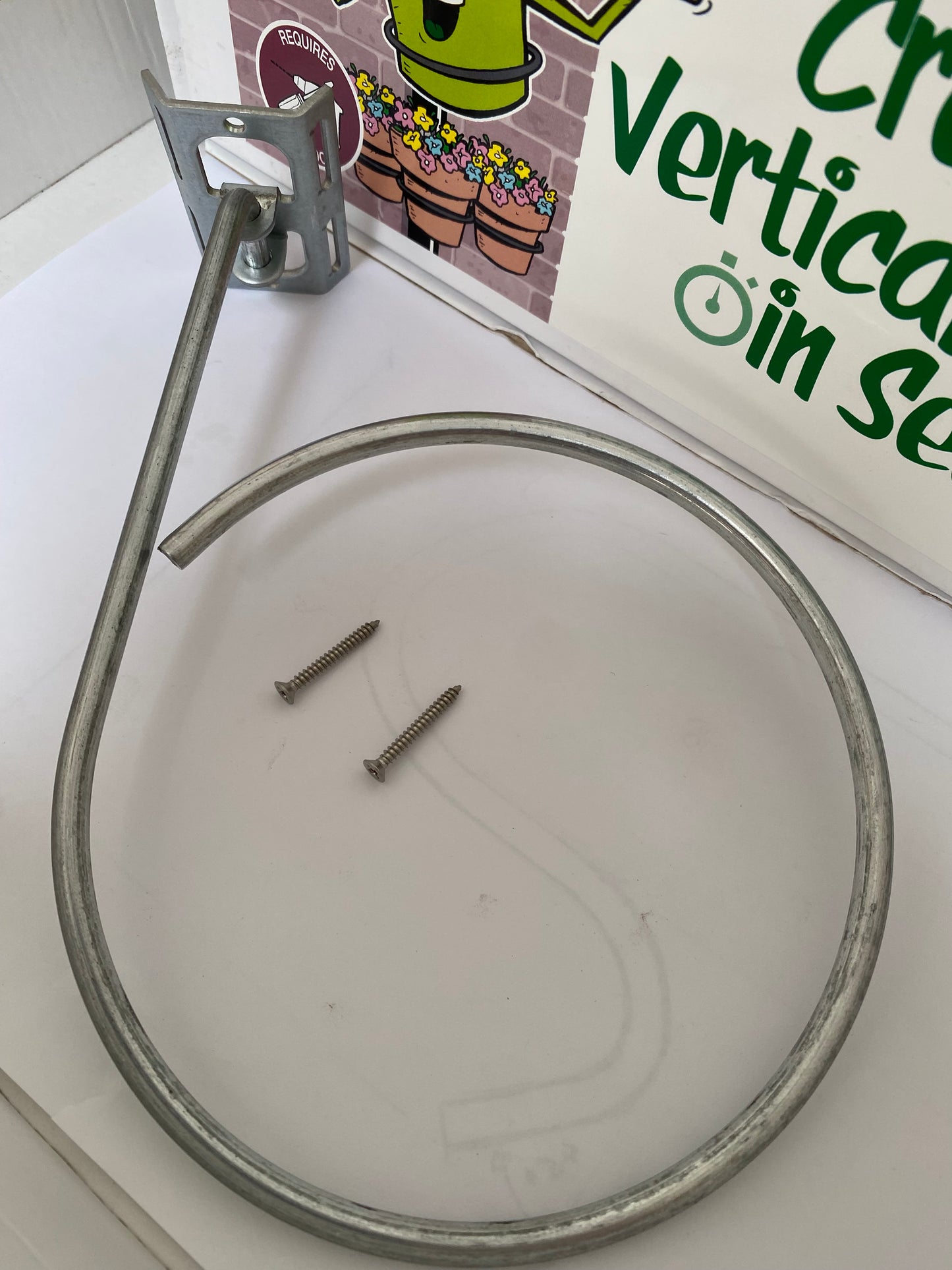 Image shows kit for wall, fence or pergola plant pot holder. Includes 1 wall mount plant pot holding ring1, 1 bracket1 and 2 screws. Plant pot holding rings can be expanded from 4-inch pot to 7-inch pot. Purchase from potmagic.co.uk. Can be quickly screw fitted to fences, pergolas and walls with screw fittings provided. Brackets are made from strong galvanised steel. Pot holding ring is made from strong 6mm diameter galvanised steel.