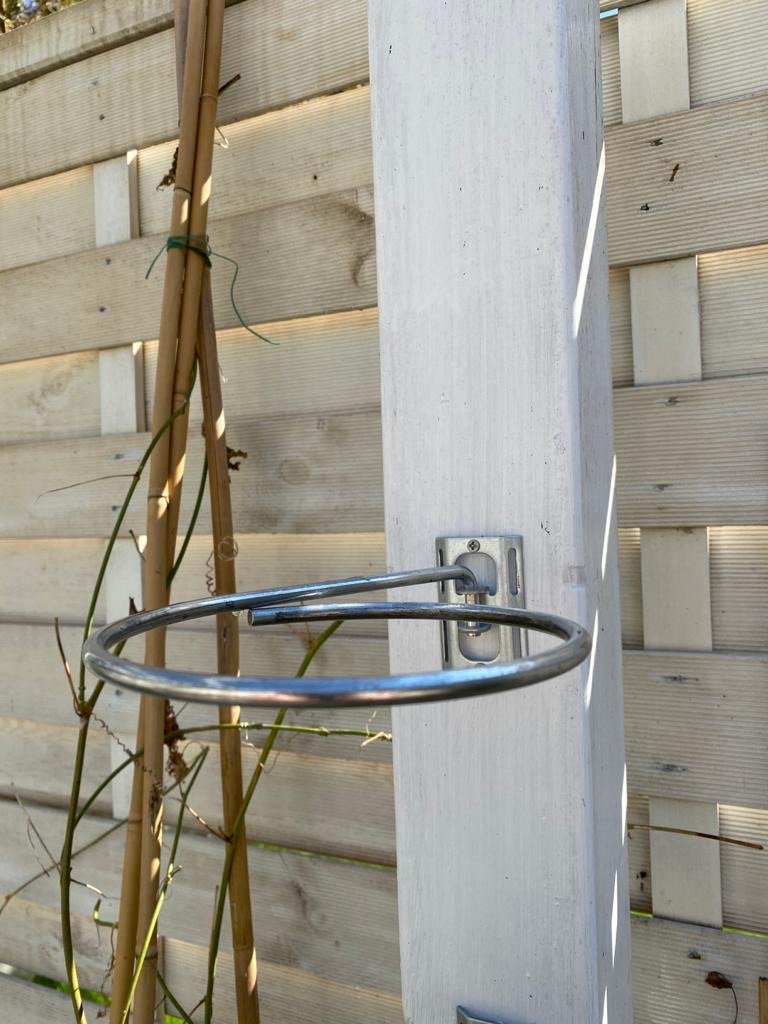 Image shows close up of 1 plant pot holder bracket fitted to a pergola post without flower pot. Available in a 3 pack for £11.75 and includes 3 plant pot holding rings, 3 brackets and 6 screws. Plant pot holding rings can be expanded from 4-inch pot to 8-inch pot. Purchase from potmagic.co.uk. Can be quickly screw fitted to fences, pergolas and walls with screw fittings provided. Brackets are made from strong galvanised steel. Pot holding ring is made from strong 6mm diameter galvanised steel.