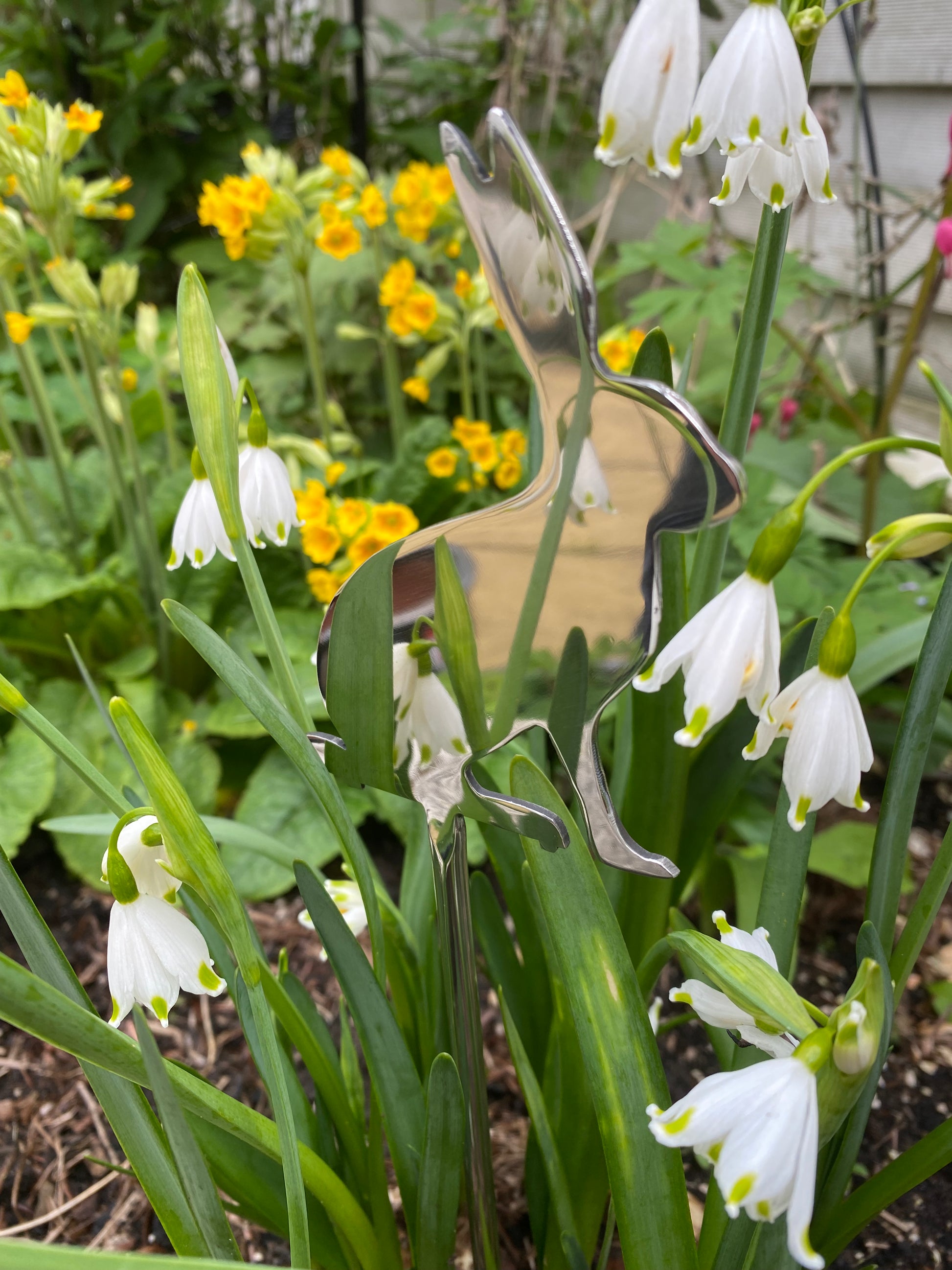 Metal butterfly sculpture among snowdrop flowers in a garden