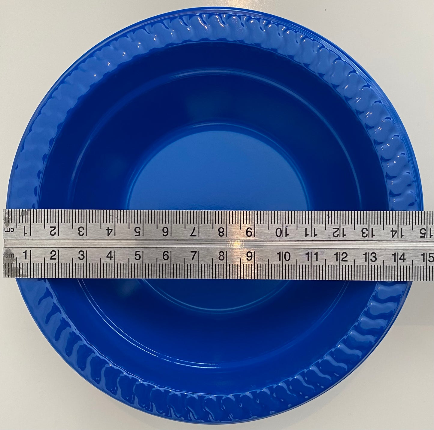 Blue plastic pan trap bowl with a ruler for scale on a white background