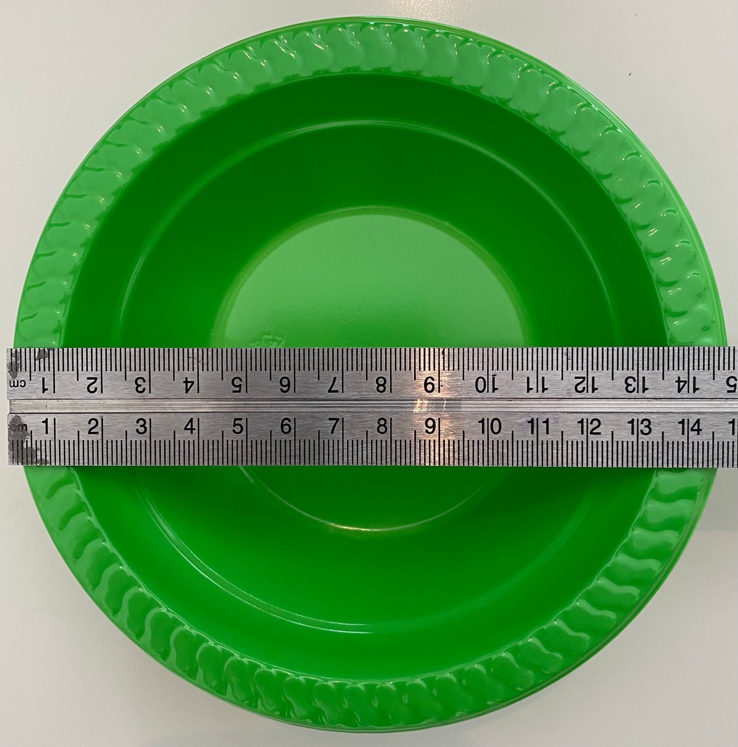 Green plastic pan trap bowl with a ruler for scale on a white background