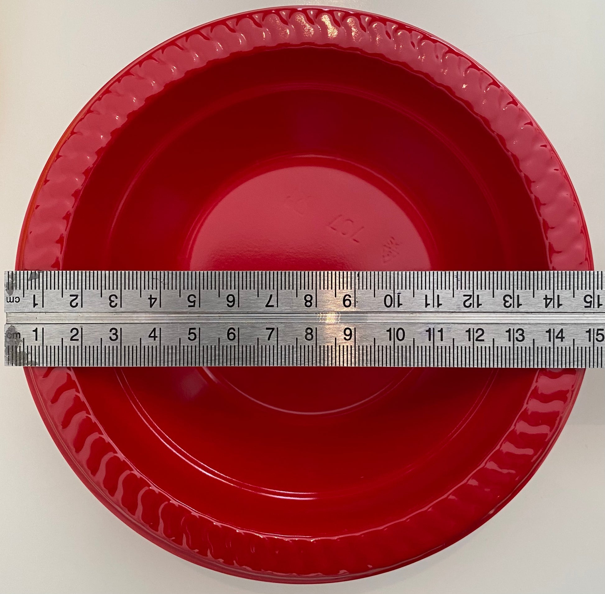 Red plastic pan trap bowl with a ruler for scale on a white background