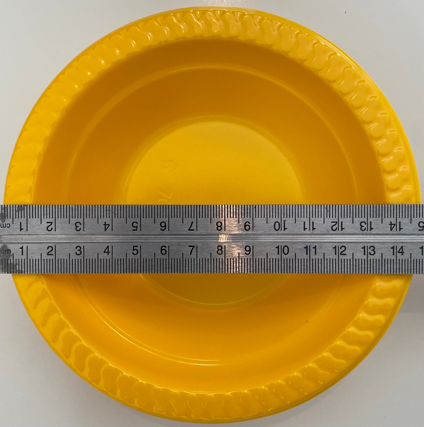 Yellow plastic pan trap bowl with a ruler for scale on a white background