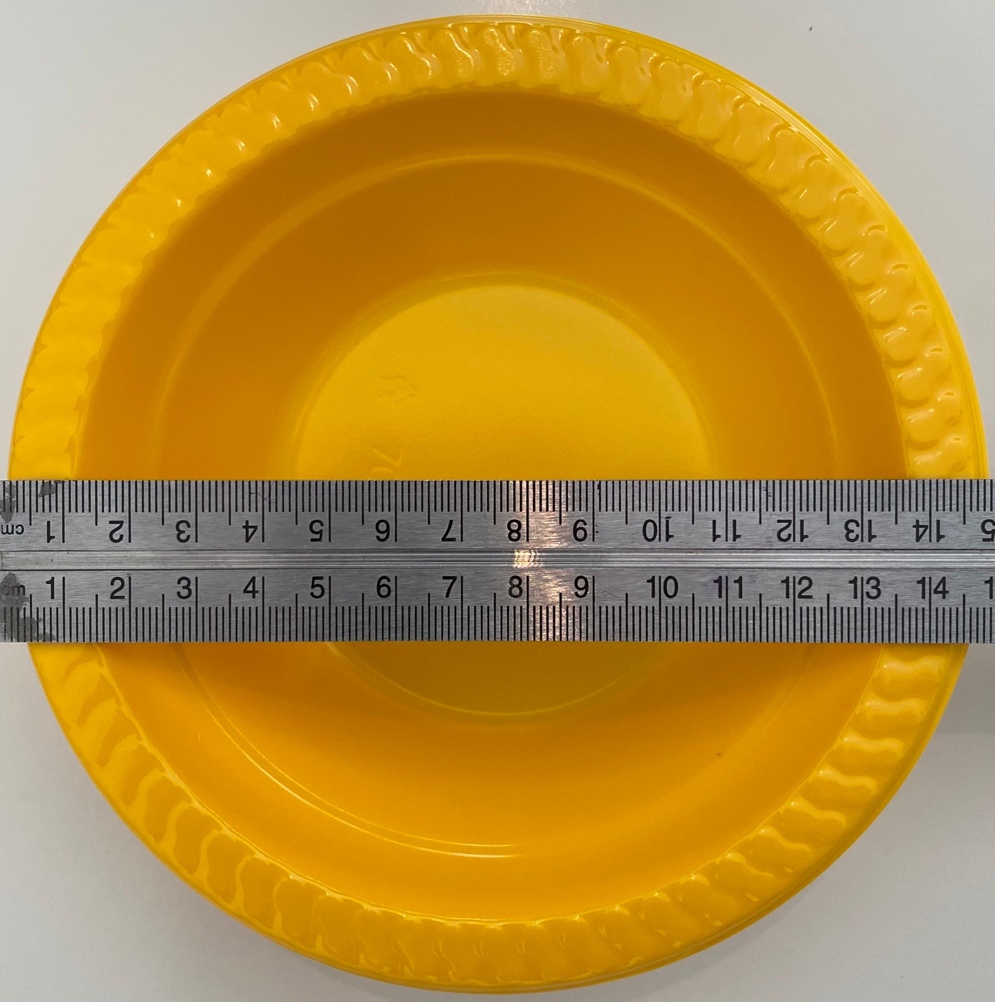 Yellow plastic pan trap bowl with a ruler for scale on a white background