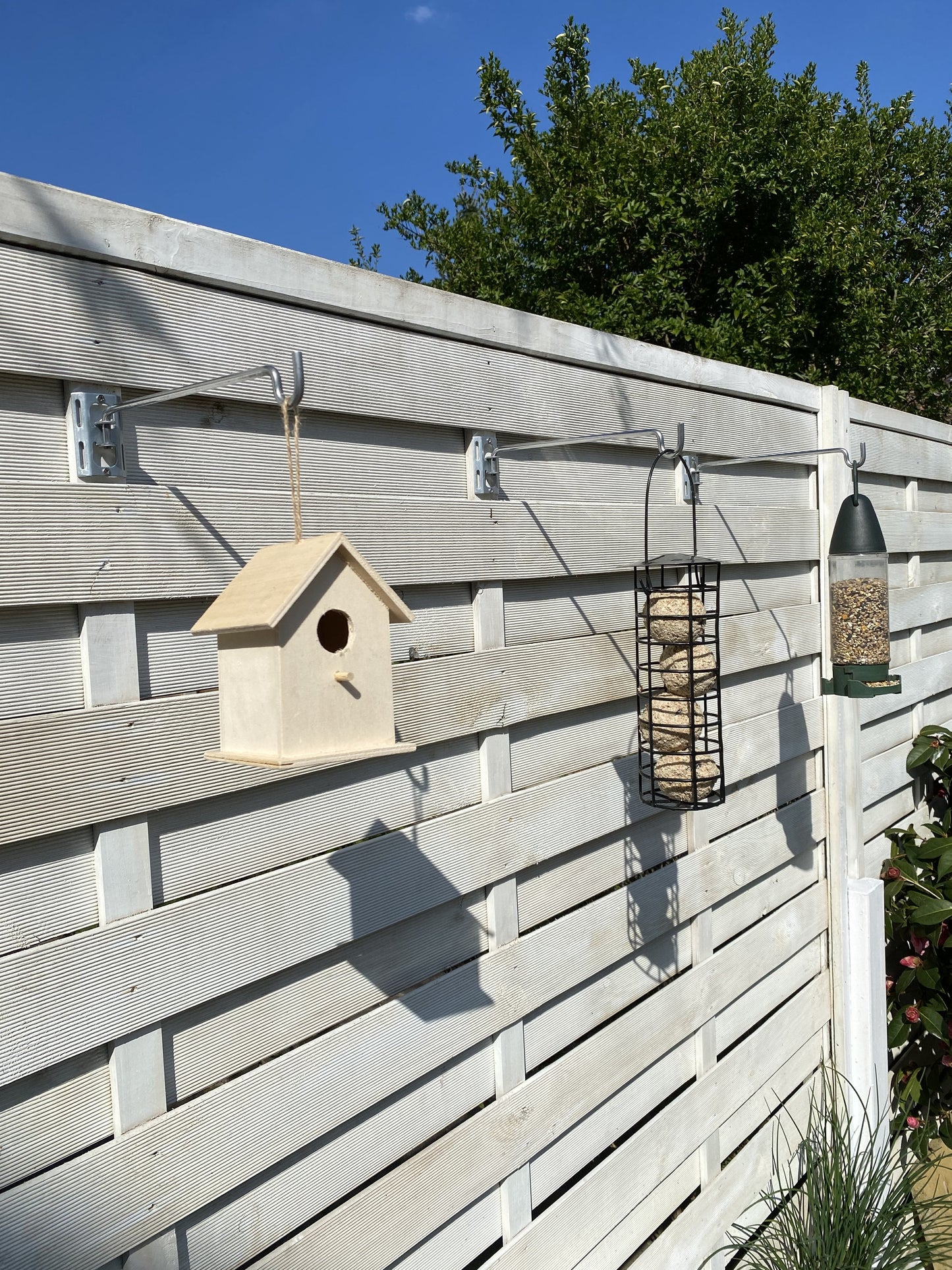 Image shows a fence with 3 bird feeder hanger bars with brackets holding a birdhouse, a seed bird feeder, and a bird fat ball feeder. Hanger bars have a deep hooked end to securely retain the feeders etc. Image shows a set 3 pack which can be fitted to fences, pergolas and walls with screw fittings provided in seconds - 3 Pack for £6.99 from potmagic.co.uk. Brackets are made from strong galvanised steel. Hook-ended hanger bar is made from strong 6mm diameter shiny galvanised steel. 
