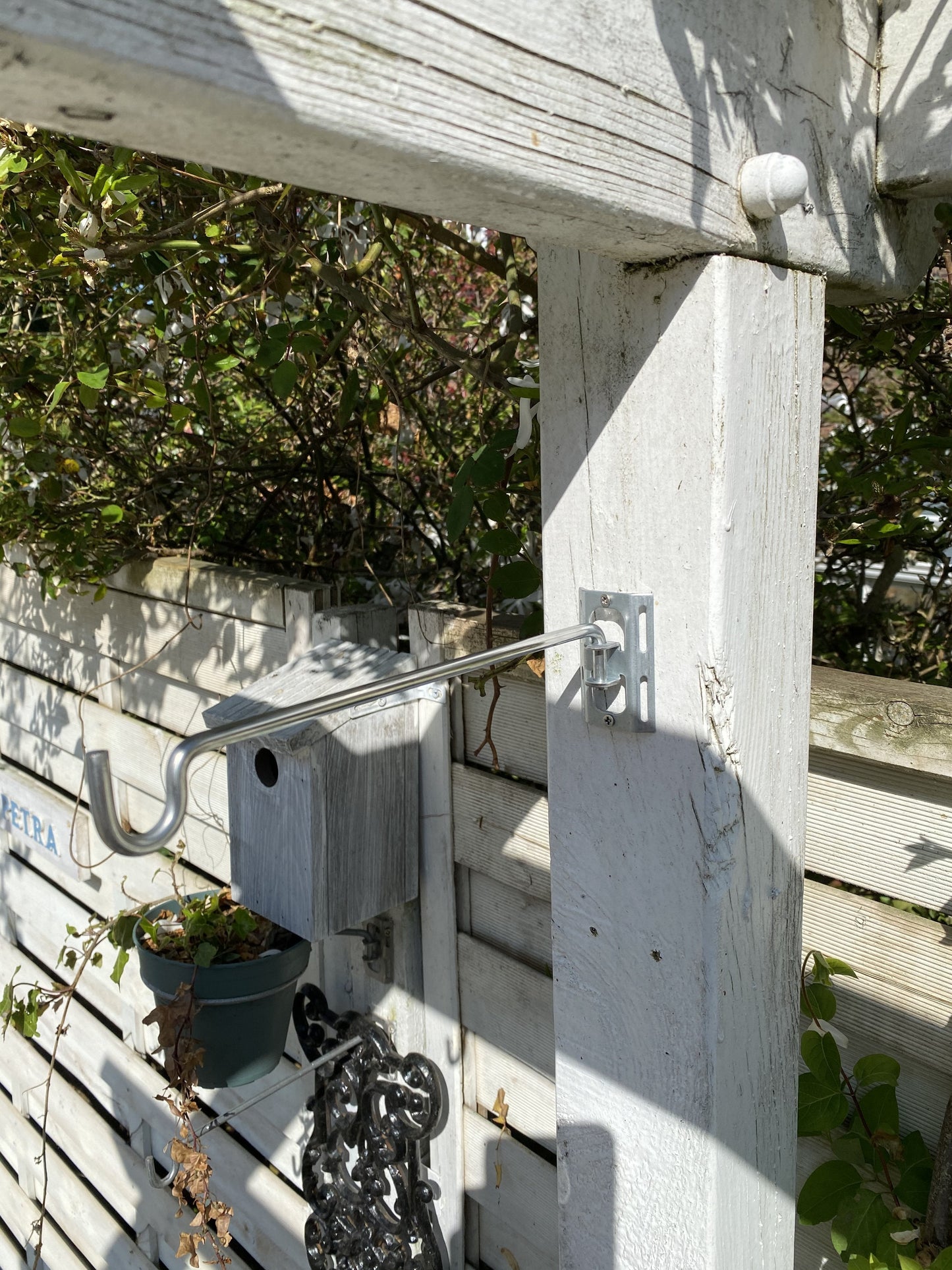 Image shows a pergola post with 1 bird feeder hanger bar with bracket closeup. Hanger bar has a deep hooked end to securely retain a bird feeder, etc. Purchased in a 3 pack for £6.99 from potmagic.co.uk. Can be screw fitted to fences, pergolas and walls with screw fittings provided in seconds. Brackets are made from strong galvanised steel. Hook-ended hanger bar is made from strong 6mm diameter shiny galvanised steel. 